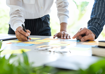 two people around a table discussing strategies with greenery in the forefront